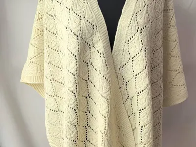 Elfenbeinfarbener Strickponcho mit offenem Rautenmuster und Blatt-Stichdetails auf schwarzer Schneiderpuppe