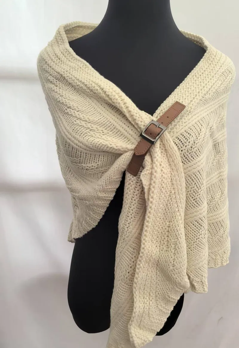 Dicker cremefarbener Zopfstrickschal mit braunem Leder-Schnallenverschluss auf schwarzer Schneiderpuppe – gemütliches Winteraccessoire
