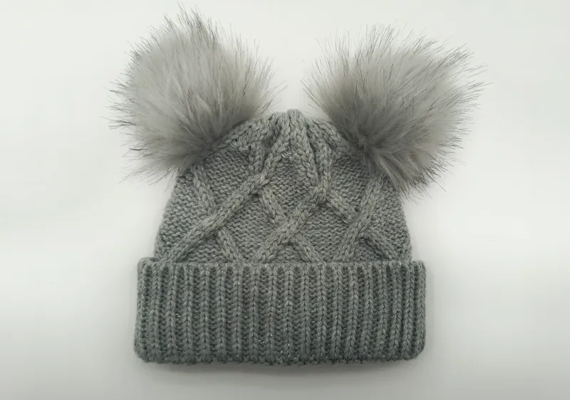 Graue Wintermütze im Zopfstrickmuster mit zwei flauschigen Kunstfell-Pompons oben und geripptem Umschlag, Flachaufnahme auf weißem Hintergrund