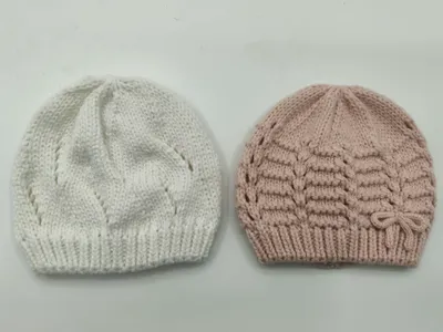 Zwei handgestrickte Babymützen nebeneinander, eine weiß mit Blattmuster und eine altrosa mit horizontaler Textur und Schleifendetail