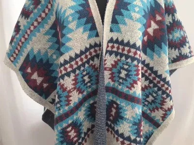 Offener Strick-Wickelponcho mit aztekischem Geometriemuster in Petrol, Burgunderrot, Marine und Creme mit Fransensaum auf Schneiderpuppe