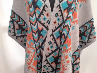 Offener Strickmantel im Boho-Stil mit geometrischem Muster in Grautönen, Petrol und Orange, mit Fransenabschluss an Saum und Ärmeln