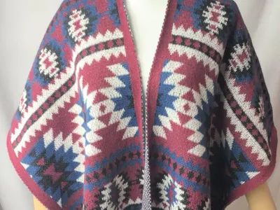 Weiter Strickponcho mit offenem Vorderteil, buntem Indianermuster in Weinrot, Dunkelblau, Weiß und Schwarz sowie Quastenborte
