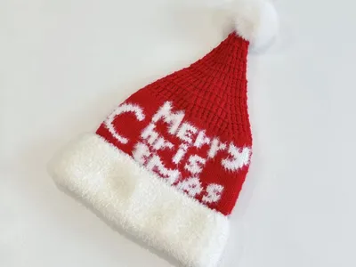 Gestrickte Weihnachtsmütze in Rot mit eingestricktem Schriftzug Merry Christmas, weißem Fellbündchen und Pompom-Spitze