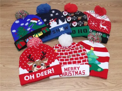 Sechs verschiedenfarbige Weihnachts-Beanies mit Pompoms und eingestrickten Motiven wie Rentier, Weihnachtsmann, Schneemann und Tannenbaum auf Holzuntergrund
