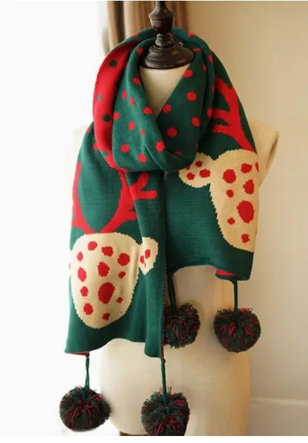 Grüner Strickschal mit Rentier-Allover-Muster und roten Punkten auf einer Schaufensterpuppe, mit dekorativen Pompom-Fransen an den Enden