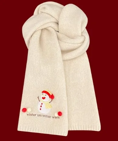 Weicher cremefarbener Strickschal mit aufgesticktem Schneemann-Motiv und roten Bommeln als Dekoration, auf dunkelrotem Hintergrund zusammengelegt