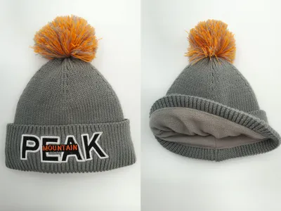 Graue Grobstrick-Wintermütze mit orangefarbenem Bommel, gesticktem Buchstaben-Patch und weichem Fleece-Innenfutter in Vorder- und Innenansicht