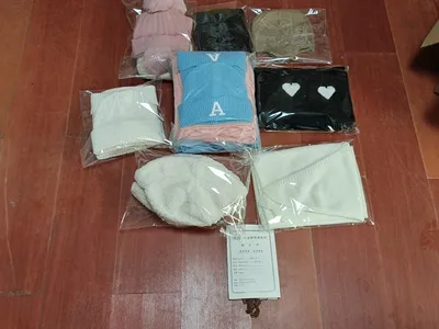 Mehrere verpackte Strickmützen und Schals in Pink, Blau, Schwarz, Creme und Beige auf Holzboden mit Produktkarte