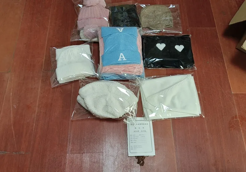 Mehrere verpackte Strickmützen und Schals in Pink, Blau, Schwarz, Creme und Beige auf Holzboden mit Produktkarte