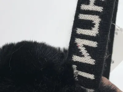 Graue flauschige Kunstfell-Ohrenschützer mit beigem Wildleder-Stirnband auf weißem Hintergrund mit Produktetikett