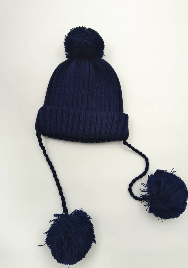 Marineblaue Winterstrickmütze mit Bommeln auf der Spitze und zwei langen geflochtenen Zopfbändern mit großen Endpompons