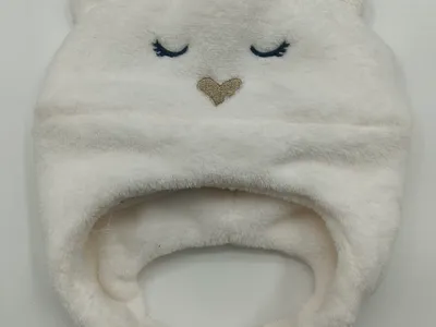 Weiches elfenbeinfarbenes Baby-Strickmützenmodell in Bärenform mit aufgestickten geschlossenen Äuglein, goldenem Herznäschen und kleinen runden Öhrchen