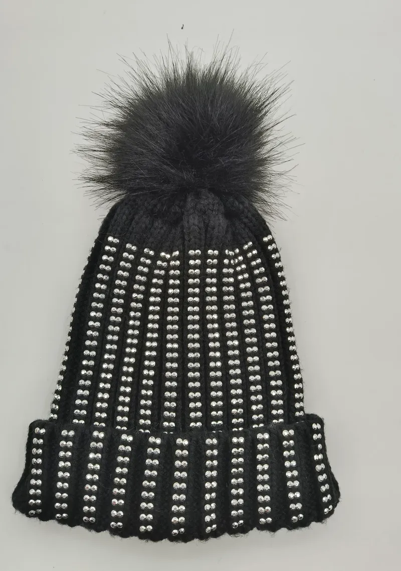 Schwarze Rippenstrickmütze dicht besetzt mit silbernen Kristallnieten und großem schwarzem Kunstfell-Bommel auf der Spitze