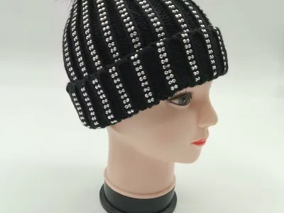 Schwarze Rippenstrickmütze mit silbernen Strassstreifen und schwarzem Kunstfell-Pompon auf Modellkopf präsentiert