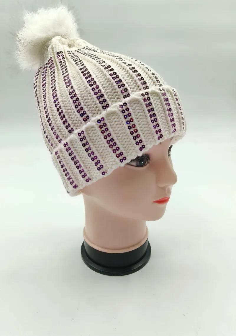 Weiße Rippenstrickmütze mit vertikalen lila Paillettenstreifen und flauschigem Kunstfell-Pompon auf Modellkopf