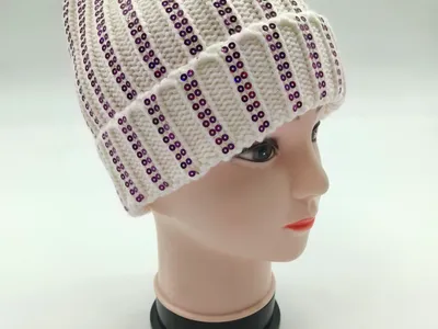 Weiße Rippenstrickmütze mit vertikalen lila Paillettenstreifen und flauschigem Kunstfell-Pompon auf Modellkopf