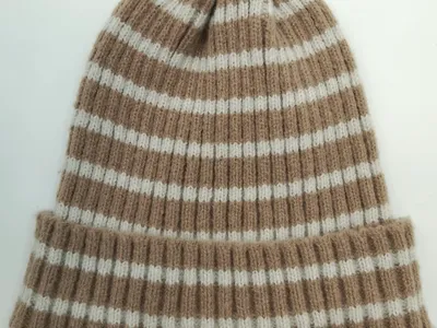 Beige-cremefarbene gestreifte Rippenstrickmütze mit umgeschlagenem Bund, flach auf weißem Hintergrund fotografiert