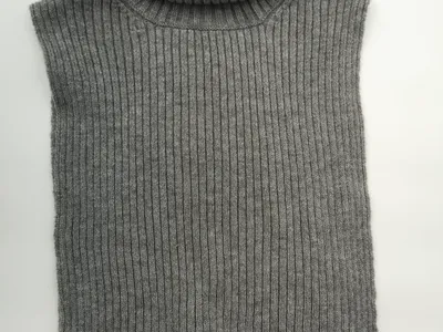 Grauer ärmelloser Rollkragen-Strickpullover in Rippenstrickoptik flach auf weißem Untergrund fotografiert