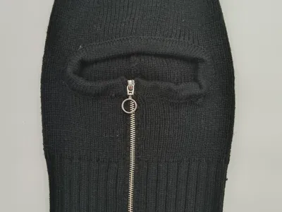 Schwarze enganliegende Sturmhaube aus Rippstrick mit silbernem Metallreißverschluss im Gesichtsbereich, flach auf grauem Hintergrund