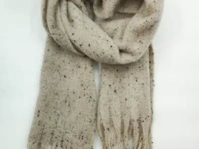 Cremefarbener Schal mit dunklen Sprenkeln aus weichem Strickgarn, locker gerollt mit Fransenzipfeln auf weißem Hintergrund
