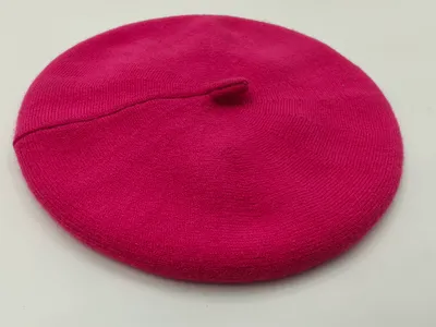Knallpinkfarbene feingestrickte Baskenmütze mit Ripprand und Mittelstielo, flach auf weißem Hintergrund fotografiert