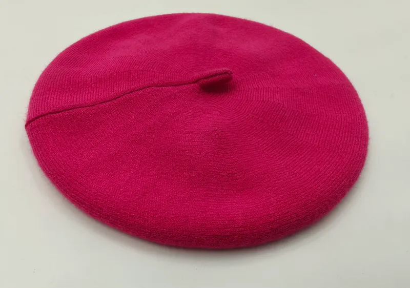 Knallpinkfarbene feingestrickte Baskenmütze mit Ripprand und Mittelstielo, flach auf weißem Hintergrund fotografiert