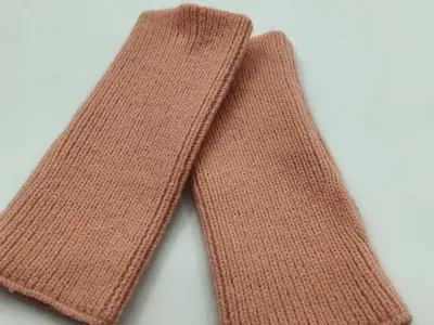 Ein Paar puderfarbene fingerlose Handschuhe aus Rippstrick flach auf weißem Hintergrund, weiche elastische Manschetten