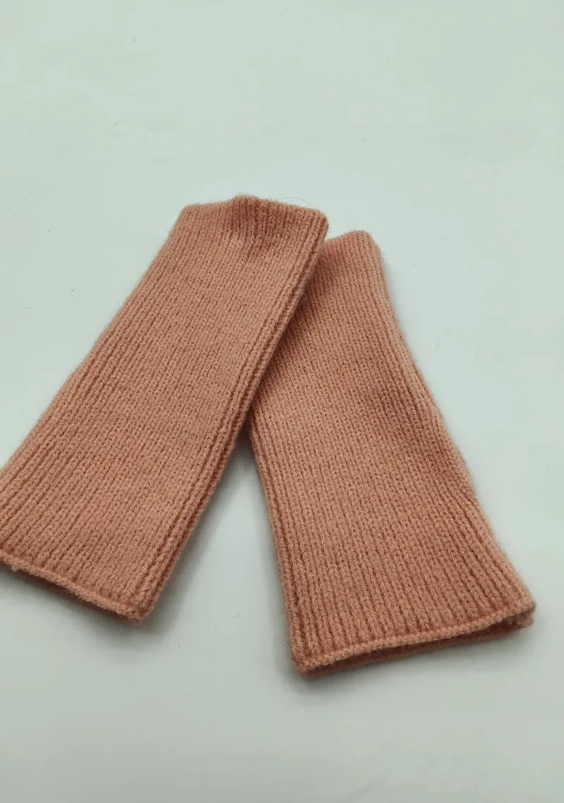 Ein Paar puderfarbene fingerlose Handschuhe aus Rippstrick flach auf weißem Hintergrund, weiche elastische Manschetten