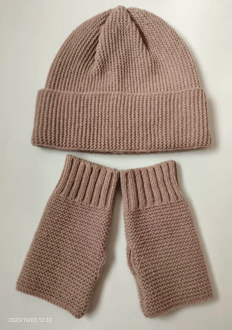 Handgestricktes Set aus altrosa gerippter Beanie-Mütze und passenden fingerlosen Fäustlingen auf weißem Hintergrund