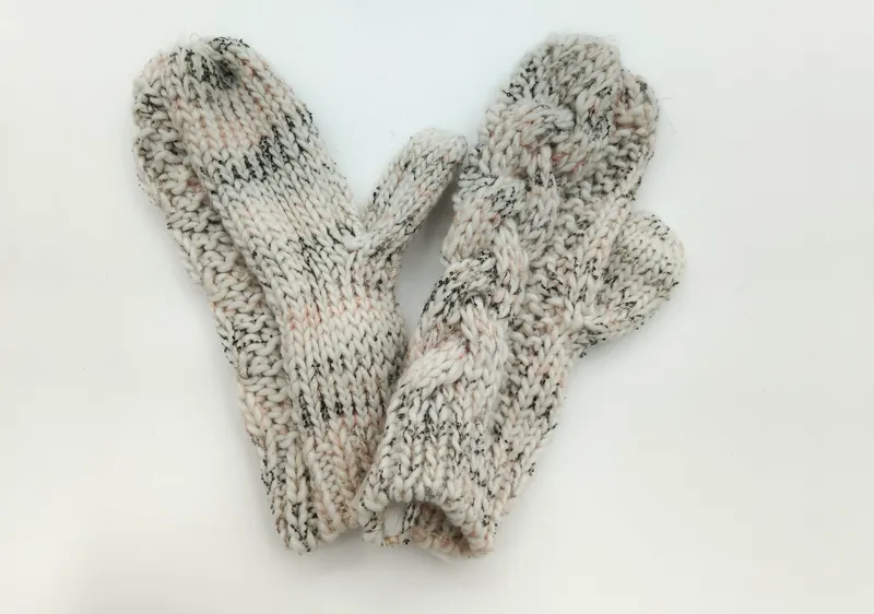 Ein Paar cremefarbene Woll-Fäustlinge mit schwarzem Tweed-Sprenkelmuster und ausgearbeiteter Daumennaht, flach ausgelegt auf weißem Hintergrund