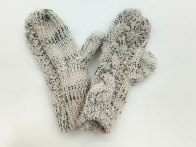 Ein Paar cremefarbene Woll-Fäustlinge mit schwarzem Tweed-Sprenkelmuster und ausgearbeiteter Daumennaht, flach ausgelegt auf weißem Hintergrund