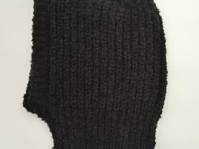 Schwarze Vollsturmhaube aus bouclétexturiertem Grobstrick, flach auf weißem Hintergrund mit fransigen Garnenden und ausgeprägter Wollstruktur