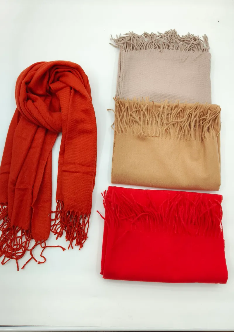 Vier zarte Schals aus Pashmina-Stoff in warmen Herbstfarben – einer locker drapiert, drei sauber gefaltet auf hellem Untergrund, mit dekorativen Fransenkanten