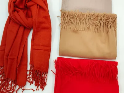 Vier zarte Schals aus Pashmina-Stoff in warmen Herbstfarben – einer locker drapiert, drei sauber gefaltet auf hellem Untergrund, mit dekorativen Fransenkanten
