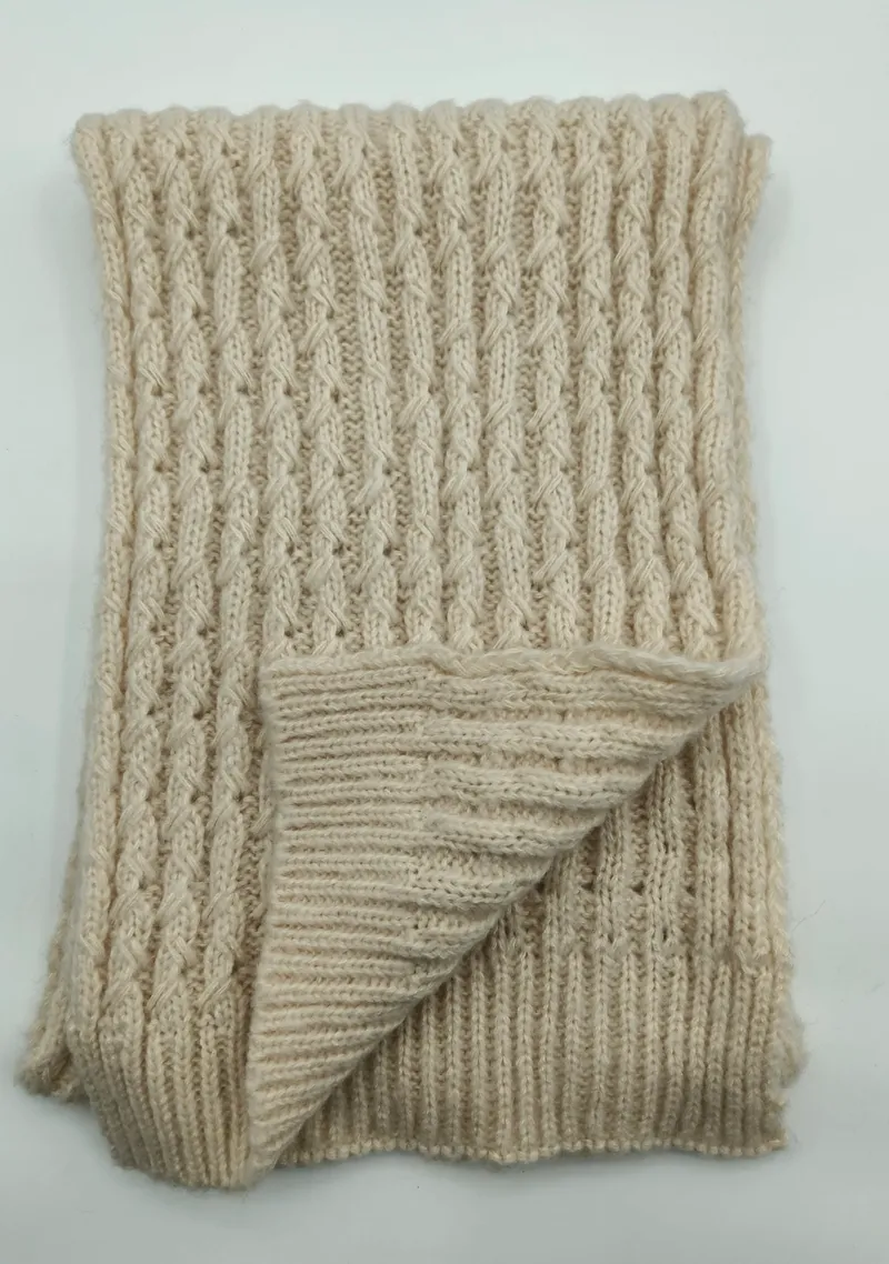 Gefaltete cremeweiße Strickdecke mit Reliefmuster aus Zopf- und Rippenstruktur auf weißem Untergrund