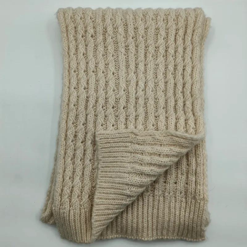 Gefaltete cremebeige Grobstrickdecke mit charakteristischem Zopf- und Rippenrelief auf weißem Untergrund