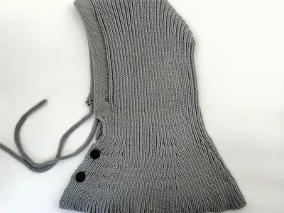 Hellgrauer Strick-Balaclava mit verstellbaren Kordeln und zwei schwarzen Knopfverschlüssen auf weißem Hintergrund