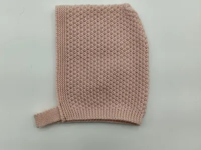 Flach gelegte, zartrosa Babymütze in Perlstricktextur mit geripptem Kinnband auf weißem Hintergrund