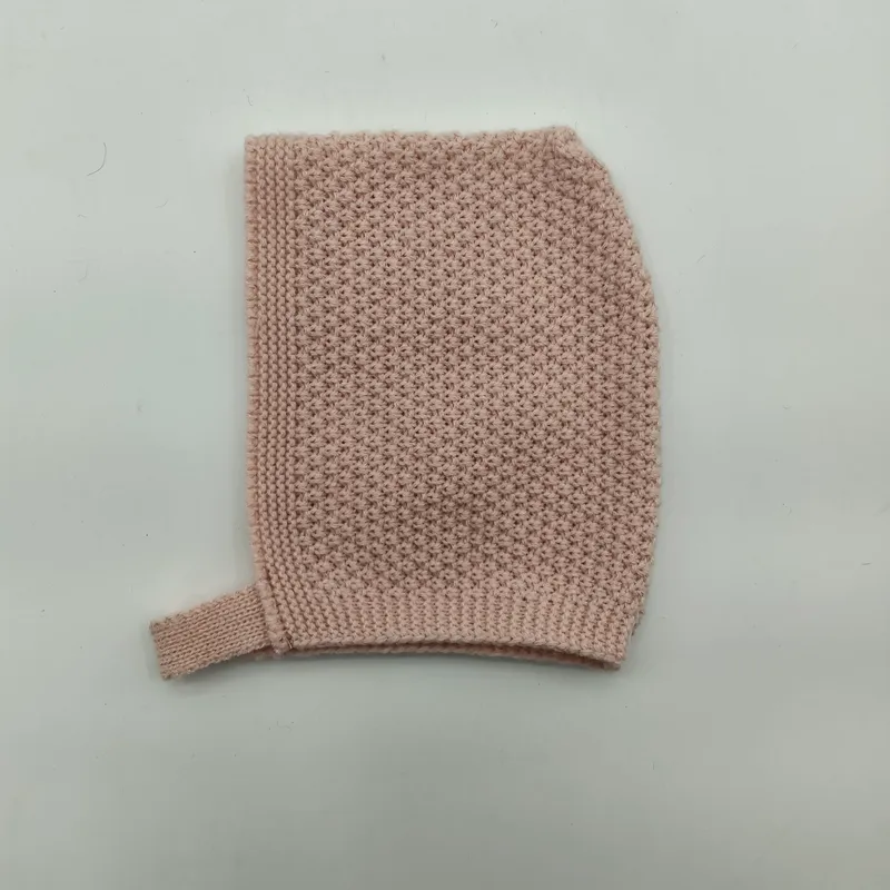 Flach gelegte, zartrosa Babymütze in Perlstricktextur mit geripptem Kinnband auf weißem Hintergrund