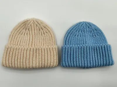 Zwei Grobstrick-Rippenbeanies flach ausgelegt – eine in Creme, eine in Himmelblau – mit umgekrempeltem Bündchen auf weißem Hintergrund