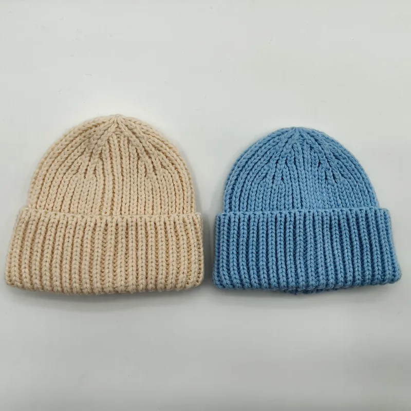 Zwei Grobstrick-Rippenbeanies flach ausgelegt – eine in Creme, eine in Himmelblau – mit umgekrempeltem Bündchen auf weißem Hintergrund