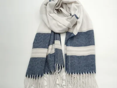 Gewebter Schal in Marineblau und Creme mit markantem Fischgrat-Muster, breiten Streifen und Quasten-Fransen, aufgerollt auf weißem Hintergrund