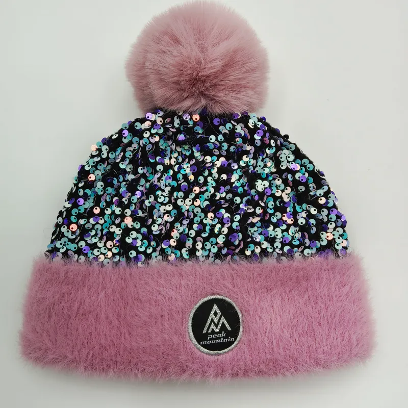 Rosafarbene Wintermütze mit schimmerndem Paillettenkörper, fluffigem Kunstpelz-Bündchen in Pink und großem Bommel auf weißem Hintergrund