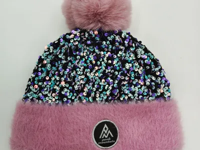 Rosafarbene Wintermütze mit schimmerndem Paillettenkörper, fluffigem Kunstpelz-Bündchen in Pink und großem Bommel auf weißem Hintergrund