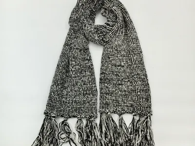 Grob gestrickter Winterschal in Schwarz-Weiß-Melange mit langen dekorativen Fransenenden, drapiert auf hellem Untergrund