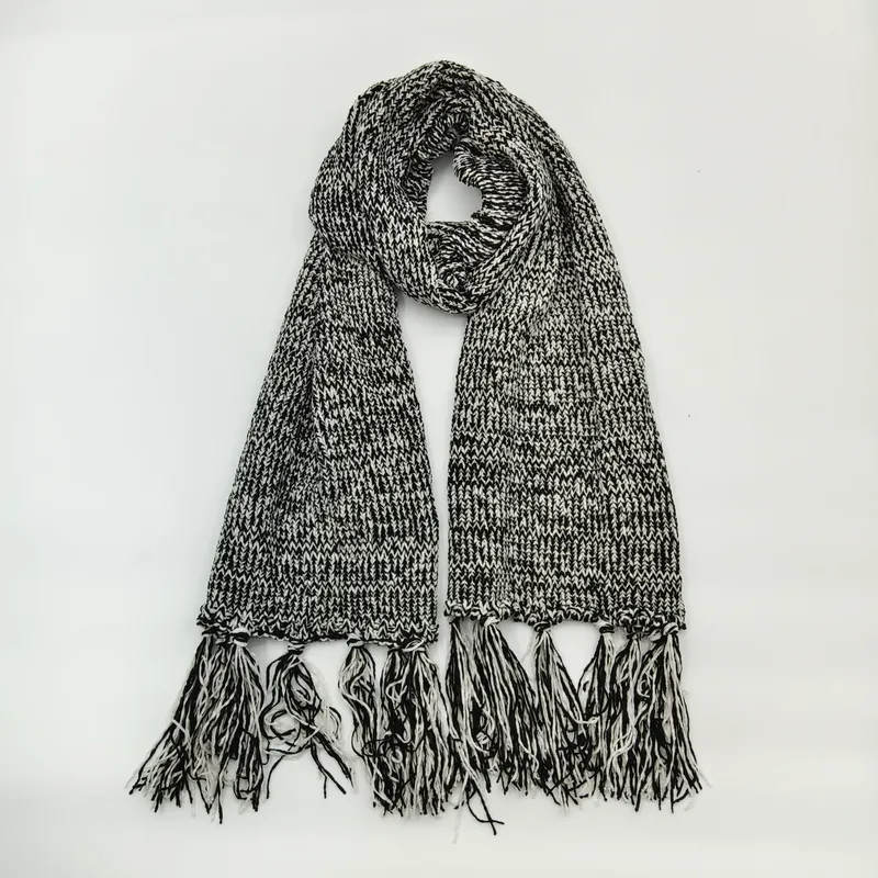 Grob gestrickter Winterschal in Schwarz-Weiß-Melange mit langen dekorativen Fransenenden, drapiert auf hellem Untergrund