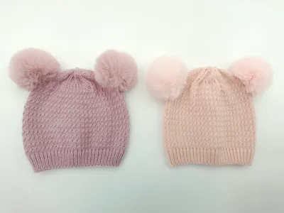 Zwei gestrickte Winterbeanies mit je zwei Kunstfell-Pompons in den Farben Flieder und Hellrosa, auf weißem Hintergrund fotografiert