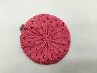 Draufsicht auf eine rosafarbene gestrickte Baskenmütze mit sternförmigen Lochstrickmustern und kleinem sandfarbenen Pompon auf weißem Grund