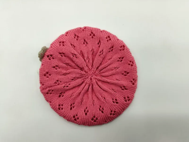 Draufsicht auf eine rosafarbene gestrickte Baskenmütze mit sternförmigen Lochstrickmustern und kleinem sandfarbenen Pompon auf weißem Grund
